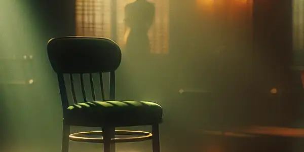 A dimly lit room with a green chair, warm lighting, and hints of intimacy in the background.